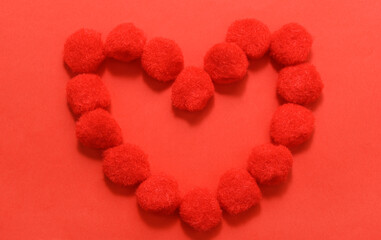Obraz premium The symbol of love is a heart made of pompoms on a red background.
