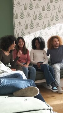 Slow motion of young multiethnic friends sitting on sofas and playing charades spending weekend together at home