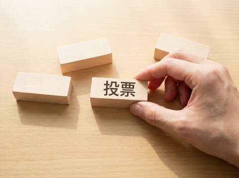 机の上で「投票」と書かれた木製ブロックに手を添える様子
