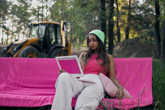 Young woman working on laptop outdoors with tractor in background