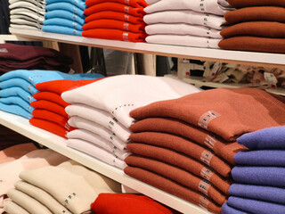 showcase stack of sweaters in the store . multi-colored knitted sweaters stacked in piles on a wooden counter in a clothing store. Seasonal Sale