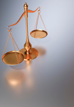 A polished brass balance scale with two empty pans hangs suspended, casting a soft shadow on a smooth, reflective surface