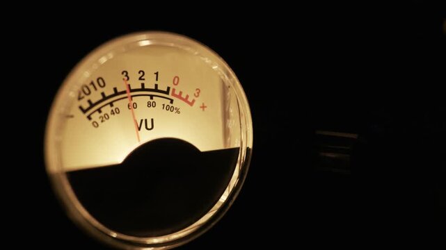 Backlit analog VU meter with a fluctuating needle measuring sound levels. Concept of audio engineering, music production, sound mixing, and vintage recording equipment.