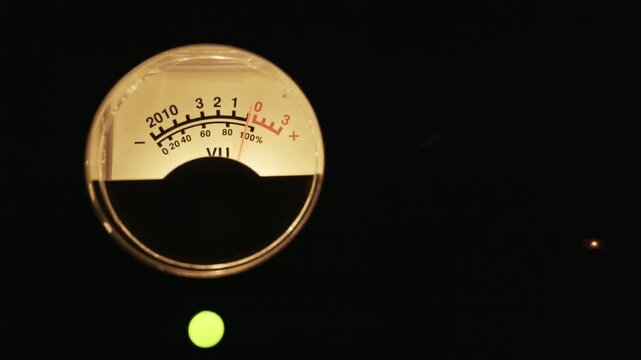 Close up of an analog VU meter with its needle fluctuating against a dark background. Concept of sound levels, audio engineering, vintage electronics, and music production.
