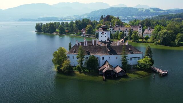 Aerial of beautiful white castle Ort Seeschloss in the Lake Traunsee, at Gmunden town. Serene lake, vibrant boats, and picturesque buildings along the shoreline. Austria tourism and scenic places