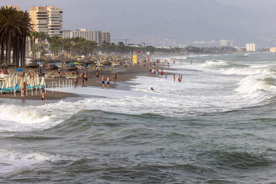 Foamy sea waves and relaxing people on the sandy beach of Carihuela in Torremolinos, Malaga, Costa del Sol, Spain