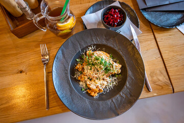 Serbian risotto with grated cheese and parsley leaf on black plate on table. Drink, beetroot salad,napkin and second plate.