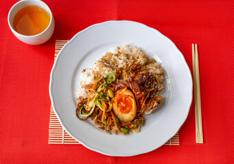 Kung pao pork belly, rice, vegetable and peanut on white plate on red.