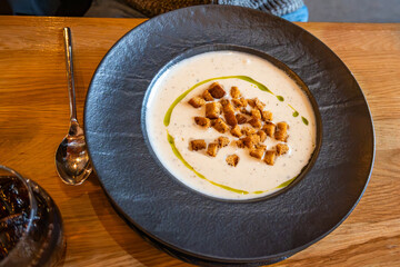 Creamy garlic soup with fried bread cubes and oil in black plate.