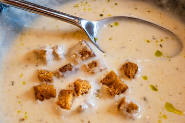 Creamy garlic soup with fried bread cube, oil and spoon.