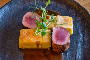 Medium pork tenderloin with cube of creamy sliced baked potato, green twig sprouted pea on blue plate.