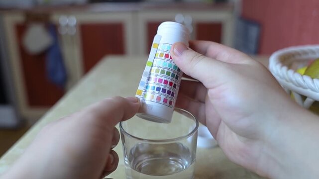 A man in the kitchen tests tap water quality with a test strip. Home testing for drinking water safety, pH, chlorine, and chemical contaminants.