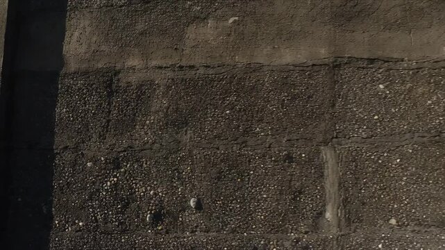 Panning camera pulling back to reveal pebble concrete wall at embankment, showing pilasters, shadow