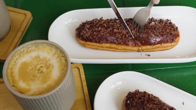 Person a cafe pastry shop eats fresh sweet eclairs cakes with cream cheese and chocolate chips, close-up of cutting an eclair.