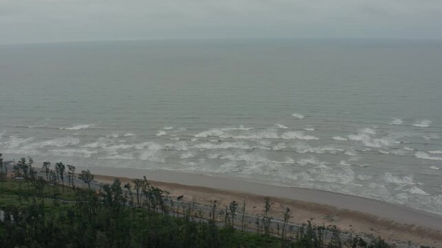 Aerial drone sweeps along Talsari Beach showcasing sandy shores gentle waves forested edges and expansive Bay of Bengal under overcast skies.