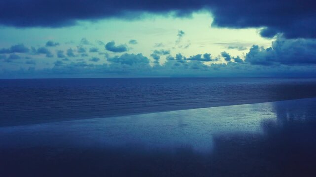 Drone moves up with wet sandy shore reflecting dramatic sunset clouds over vast Bay of Bengal horizon.