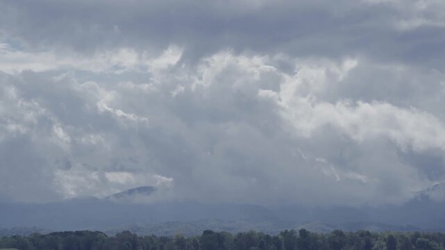 A dramatic landscape shot of heavy storm clouds moving over distant mountains and a forest line in the Posavje region of Slovenia.