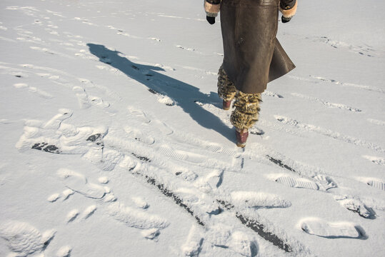 Female legs in boots walking away on fresh snow in winter. Walking on snow in winter coat and fur boots, close-up of footsteps and clothing texture