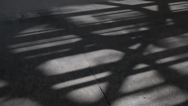 Moving overhead shadows casting oval patches and linear bands on concrete slabs, sunlight shifting