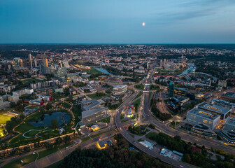 Fototapeta premium Aerial drone view of Vilnius city center during a summer blue hour, featuring a Japanese garden, the Neris River, modern skyscrapers, and the Park Town business district.