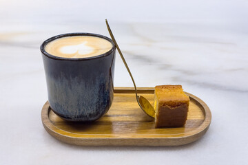 cup of aromatic coffee with a piece of biscuit on a wooden tray on a white table close-up