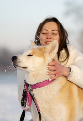 A woman hugs an Akita dog in a snowy landscape, both smiling and enjoying the moment