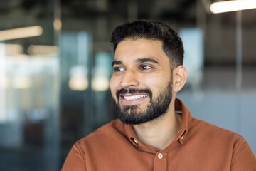 Fototapeta premium Bearded professional man smiling confidently, looking towards the future in a corporate office setting, representing success, positivity, and a thriving career