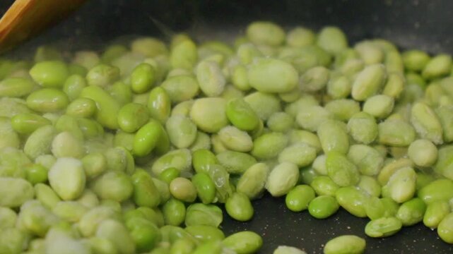 Green beans are being cooked in a frying pan on a stove.