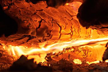 Image shows burning coals and ashes in a stove or fireplace. Selective focus