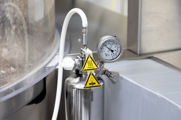 A close-up view of a stainless steel industrial pressure gauge and control valve with hot warning...