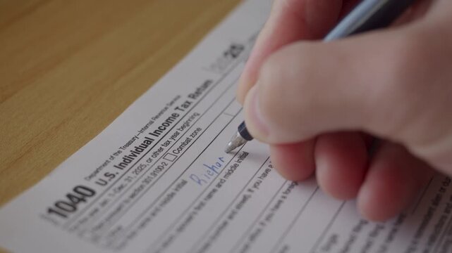 Man Filling In The Tax Form 1040 for 2025 Year. Person Calculates of Planning Budgets Yearly Personal Finance and Fills up US Tax Form 1040 For 2025 Year. Signing 1040 Income Tax Return For 2025 Year.