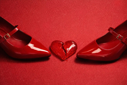 Glossy red shoes framing broken glass heart on textured red backgroud. Fashion still life, dramatic mood, bold color focus. Valentines day concept