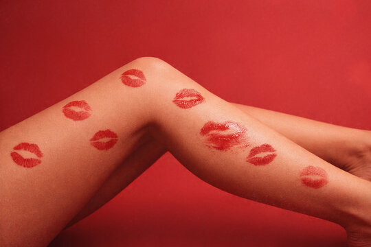 Female legs covered with red lipstick kiss marks against rich red background. Playful body detail, bold color contrast, fashion still life with provocative mood. Valentine&rsquo;s Day concept.