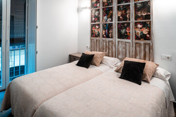 Bedroom interior featuring twin beds with beige bedding and a unique headboard crafted from old doors with floral wallpaper panels