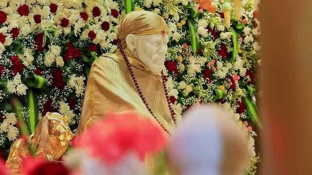 A closeup video of Sai Baba or Sai Ram idol surrounded by floral decorations inside the temple