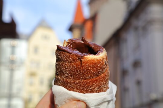 Czech cuisine. Trdelnik chimney cake with cinnamon, sugar and chocolate spread inside. Prague city in background.