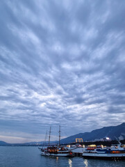 Fototapeta premium Docked sailboats and city lights at evening harbor with cloudy sky