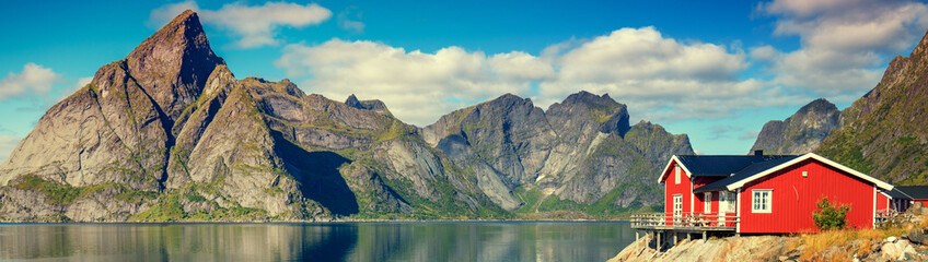 Beautiful fishing village on fjord. Beautiful nature with blue sky, reflection in water, rocky beach and fishing house (rorby). Lofoten, Reine, Norway