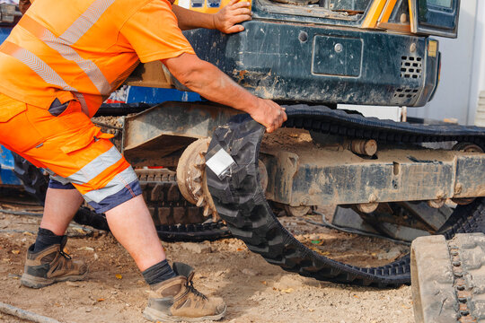 Construction machinery excavator repaired by mechanic and new rubber track being fitted to it on construction site