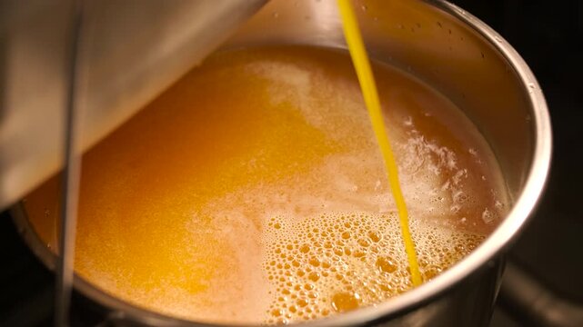 Industrial process of pouring orange juice concentrate into a stainless steel tank. Manufacturing of sweet fruit beverages at a food factory.