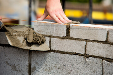 Construction worker bricklayer lays bricks for new structure at building site using tools and...