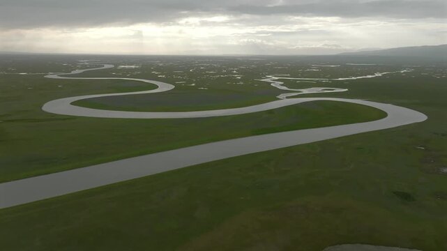 Aerial view of a serpentine river snaking through lush, green grassland under a cloudy sky creating a mesmerizing contrast of colors and textures, Ba Yin Guo Leng Meng Gu Zi Zhi Zhou, China.