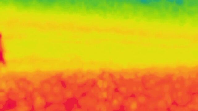 A man walks along a heated stone wall. Image from thermal imager device.