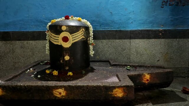 A panoramic video of historical lingam or shiv ling decorated with flowers inside the old temple