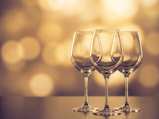 Three elegant empty wine glasses on reflective surface with bokeh