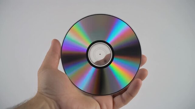 Hand holding shiny multicolored optical disc against plain gray background for data storage or music