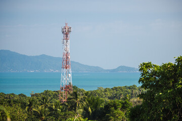 Telecommunication tower above tropical forest overlooking turquoise sea and distant island hills under clear sky