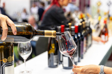 Wine tasting at winery or food and drink exhibition, sommelier pouring red wine for guests, showcasing viticulture, hospitality, gourmet experience, and beverage industry culture © Mihajlo Maricic