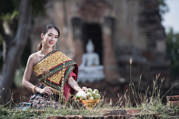Beautiful Thai Woman in Traditional Dress at the Temple. beautiful Thai woman wearing traditional Thai dress, adorned with elegant jewelry and holding a jasmine garland, standing in front of a temple
