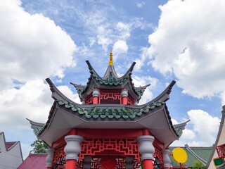 Obraz premium The roof of a traditional Chinese garden pavilion under bright cloudy blue sky, featuring red pillars and curved rooflines, reflecting East Asian cultural heritage and classical architectural design.